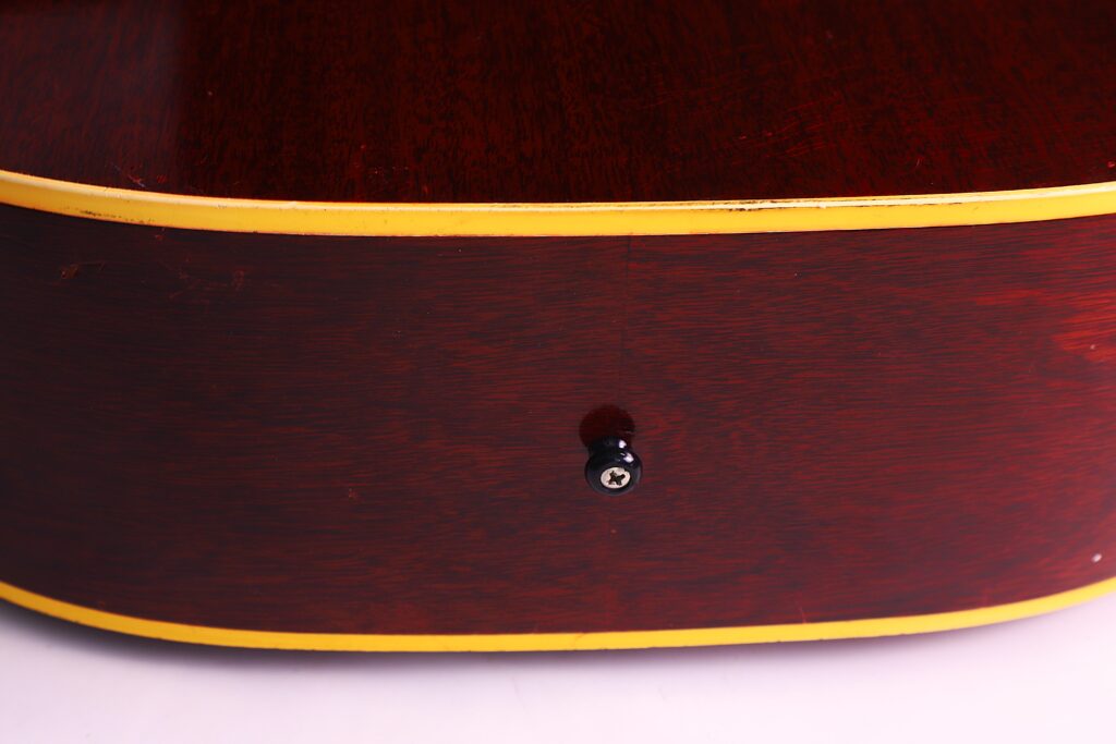 Nahaufnahme Der Seite Einer Gibson J-45 1962 Akustik-Gitarre Mit Rötlich-Braunem Holzfinish, Gelben Zierleisten Und Einem Einzelnen Gurtknopf In Der Mitte.