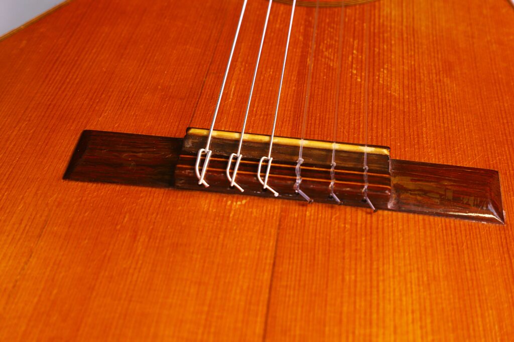 Nahaufnahme Des Holzstegs Und Der Nylonsaiten Der Julián Gómez Ramírez 1933 Klassische Gitarre. Hervorzuheben Sind Die Glänzende Oberfläche Des Korpus Und Die Detaillierte Holzmaserung.