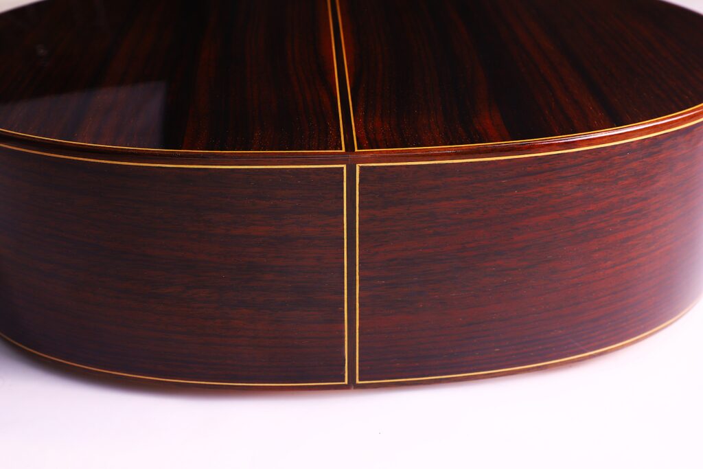Nahaufnahme Des Bodens Und Der Zarge Der José Ramírez Rb-A 636 Klassische Gitarre, Die Eine Reiche Dunkle Holzmaserung Mit Glänzender Oberfläche Und Auffälligem Gelbgoldenem Einband Entlang Der Nähte Aufweist.