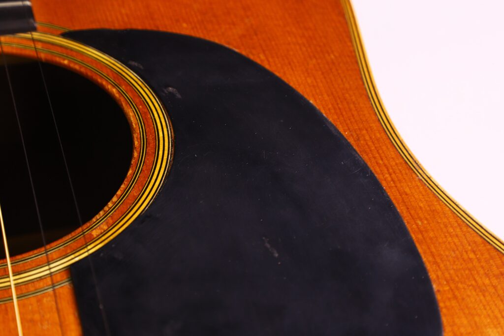 Nahaufnahme Des Schalllochs, Der Saiten Und Des Schwarzen Schlagbretts Der Martin D-28 1971 Akustik Gitarre Auf Dem Holzkorpus, Wobei Ein Teil Der Gitarre Aus Dem Rahmen Herausragt, Vor Einem Weißen Hintergrund.