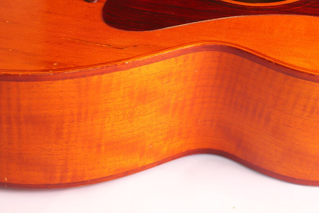 Nahaufnahme Der Seite Einer Lowden F-9 1980 Akustik-Gitarre, Die Den Orange-Braunen Holzkorpus, Die Sichtbare Holzmaserung Und Die Sanften Kurven Vor Einem Weißen Hintergrund Hervorhebt.