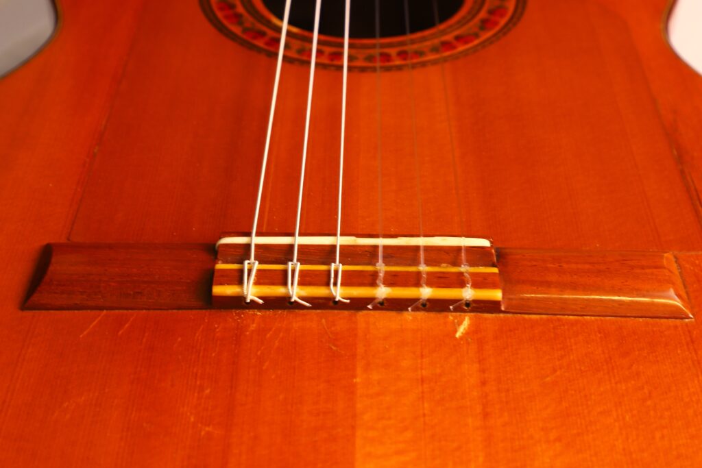 Nahaufnahme Des Stegs Und Der Unteren Saiten Einer Lester Devoe 1996 Negra Flamenco Gitarre. Hervorzuheben Sind Die Holzmaserung, Saitenäste Und Ein Teil Der Schalllochrosette.