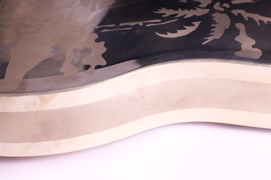 Eine Nahaufnahme Der National Reso-Phonic Style O 2009 Akustik Gitarre Zeigt Ihren Gewellten, Polierten Metallkorpus Mit Eingravierten Palmenähnlichen Motiven, Die Von Cremefarbenen Und Silbernen Schichten Umrandet Sind, Vor Einem Weißen Hintergrund.