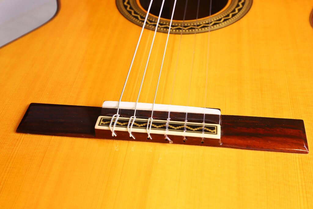 Nahaufnahme Der Saiten, Des Stegs Und Der Schalllochrosette Der José Ramírez Rb-A 636 Klassische Gitarre, Einer Klassischen Akustikgitarre Mit Holzkorpus Und Hochglanzlackierung.