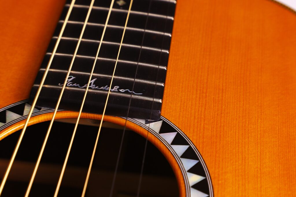 Nahaufnahme Des Halses Und Des Korpus Der Martin 0-28 Ian Anderson Akustik Gitarre Mit Sechs Saiten, Einem Partiellen Schallloch Mit Einer Dekorativen Rosette, Einer Signatur Auf Dem Griffbrett Und Einer Warmen Orange-Braunen Holzoberfläche.