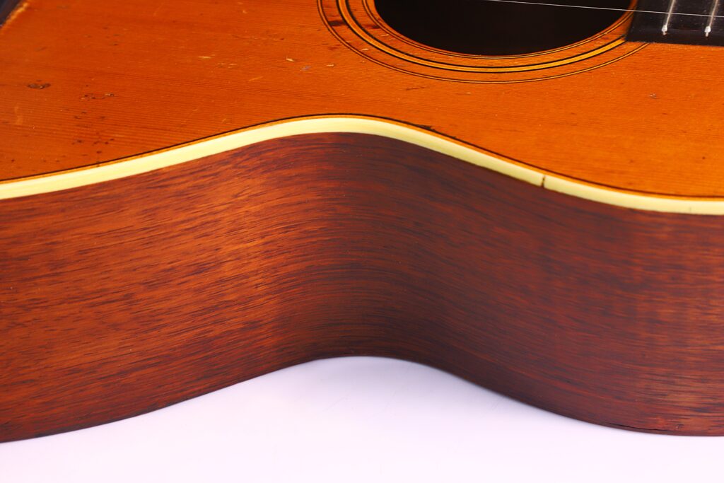 Nahaufnahme Des Korpus Einer Washburn 1894 Parlor Akustik Gitarre Mit Der Gewölbten Holzseite, Dem Schallloch, Einem Teil Der Saiten, Dem Warmen Braunen Holz Mit Sichtbarer Maserung Und Der Cremefarbenen Zierleiste.