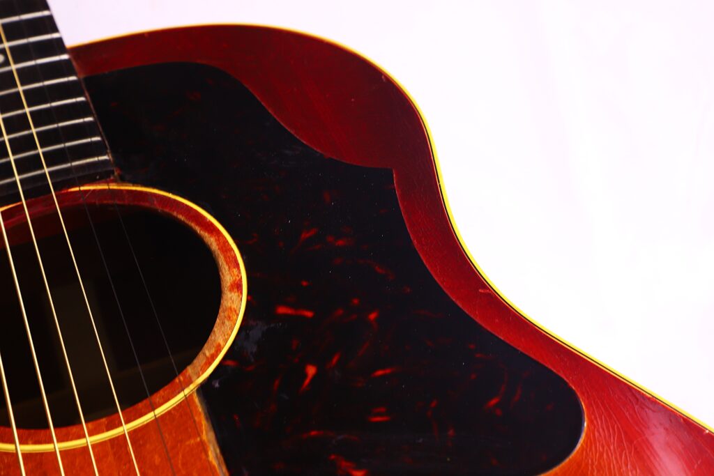 Nahaufnahme Des Korpus Einer Gibson J-45 1962 Akustik Gitarre, Wobei Die Saiten, Das Schallloch, Das Dunkle Schlagbrett Und Die Rötlich-Braune Holzoberfläche Vor Einem Hellen Hintergrund Hervorgehoben Werden.