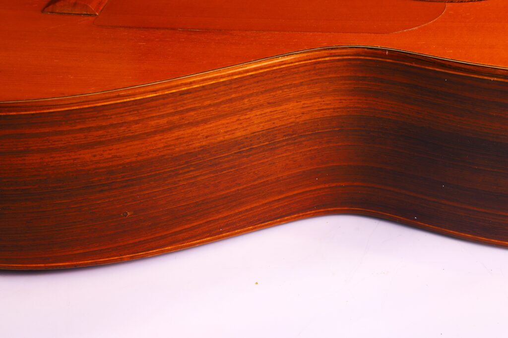 Nahaufnahme Der Gebogenen Holzseite Der Lester Devoe 1996 Negra Flamenco Gitarre, Die Die Holzmaserung Und Die Glatte Oberfläche Vor Einem Weißen Hintergrund Zeigt.