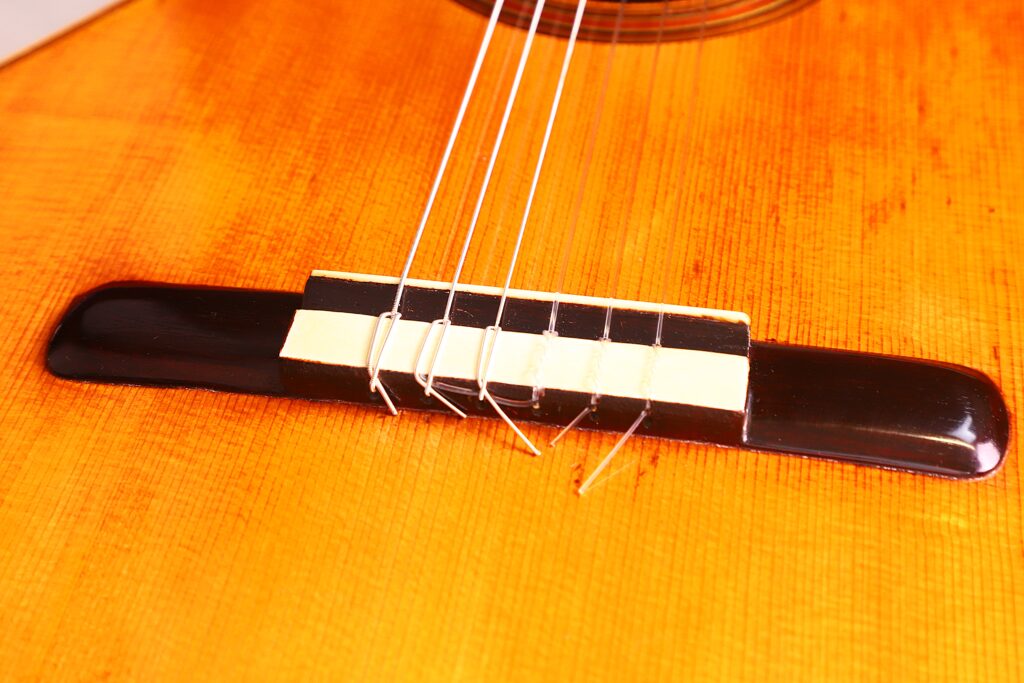 Nahaufnahme Des Stegs Der Vicente Tatay Alabau 1920 Klassische Gitarre Mit Nylonsaiten. Hervorzuheben Sind Die Detaillierte Maserung Des Holzes Und Die Saitenanordnung Über Dem Sattel.