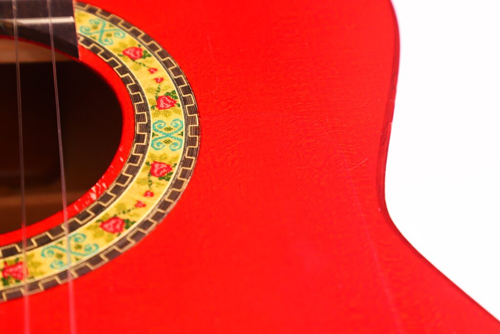 Nahaufnahme Einer Manuel Guillena 2017 Blanca Flamenco-Gitarre In Leuchtendem Rot, Die Einen Teil Des Schalllochs Mit Einem Gelb Und Grün Gemusterten Ring Zeigt, Sowie Einen Teilweise Sichtbaren Korpus Und Saiten Vor Weißem Hintergrund.