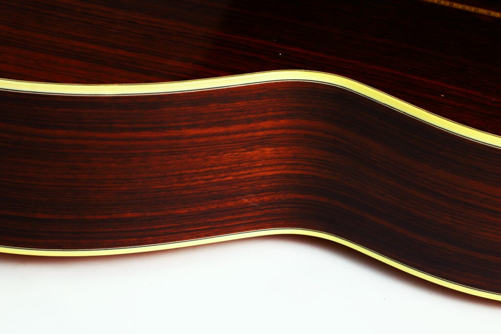 Nahaufnahme Der Seite Einer Martin 0-28 Ian Anderson Akustik-Gitarre, Die Das Holzmaserungsmuster Und Die Gelbe Zierleiste Entlang Der Gebogenen Kante Vor Einem Weißen Hintergrund Hervorhebt.