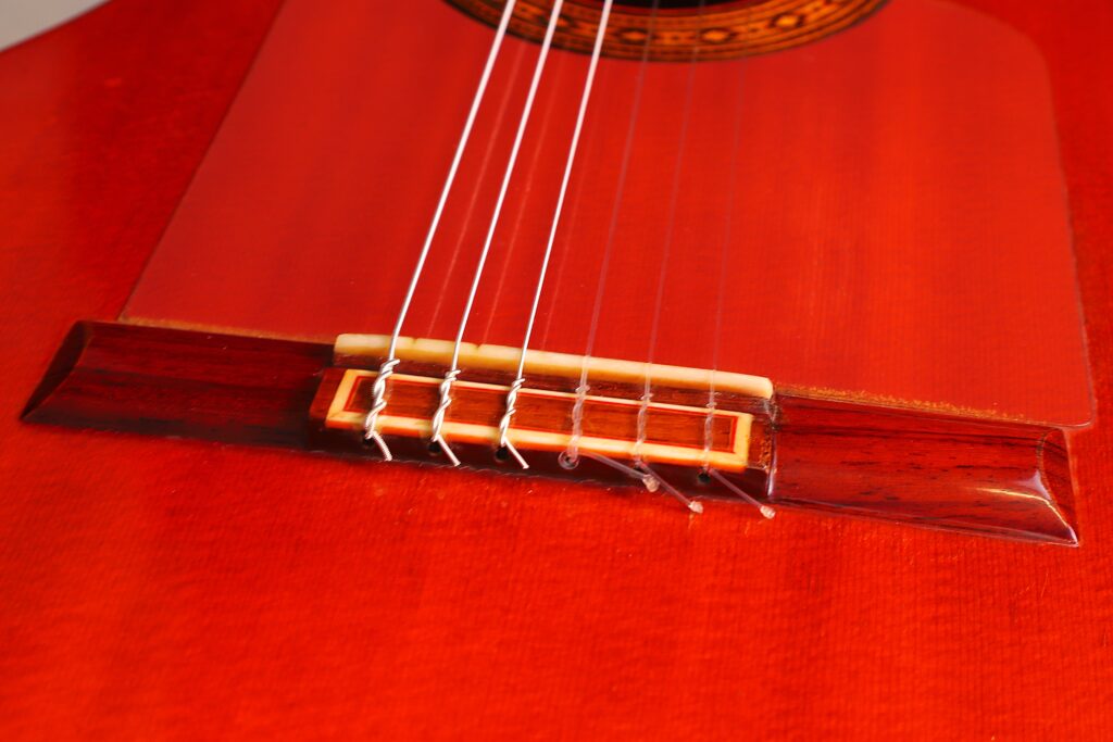 Nahaufnahme Des Glänzenden, Rot-Orangefarbenen Korpus Der Hermanos Conde 1983 Faustino Conde Flamenco-Gitarre Mit Weißen Nylonsaiten, Die An Den Dunklen Holzsteg Gebunden Sind.