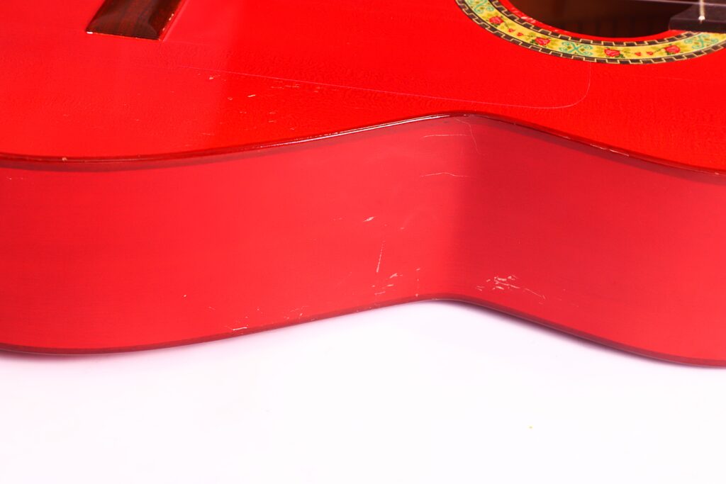 Nahaufnahme Der Seite Einer Leuchtend Roten Manuel Guillena 2017 Blanca Flamenco-Gitarre, Die Leichte Kratzer Und Einen Teil Des Schalllochs Mit Dekorativer Rosette Zeigt, Die Auf Einer Weißen Oberfläche Ruht.