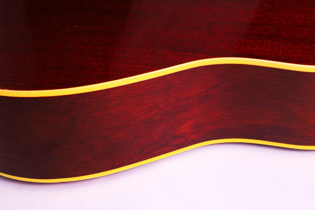 Nahaufnahme Der Seite Einer Gibson J-45 1962 Akustik-Gitarre, Die Ein Sattes Rotbraunes Holzfinish Mit Gelben Verzierungen Vor Weißem Hintergrund Aufweist.