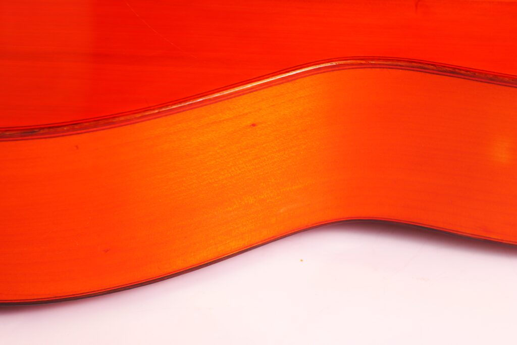 Nahaufnahme Der Seite Einer Faustino Conde Flamenco-Gitarre Von Hermanos Conde Aus Dem Jahr 1983. Hervorzuheben Sind Die Glatte, Glänzende Orange-Braune Holzmaserung Und Die Eleganten Rundungen Vor Einem Weißen Hintergrund.