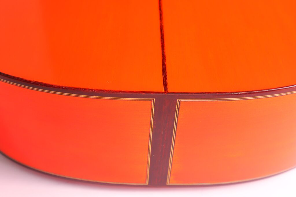 Nahaufnahme Des Hell Polierten Orangefarbenen Bodens Und Der Kante Der Pedro Fernández Luque 2020 Blanca Flamenco Gitarre, Die Die Feine Holzmaserung, Die Sauberen Nähte Und Die Komplizierten Einlegearbeiten Hervorhebt.