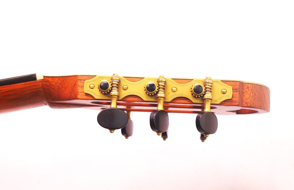 Seitliche Nahaufnahme Der Kopfplatte Der Mario Gropp 2020 Klassische Gitarre Mit Drei Goldenen Stimmwirbeln Mit Schwarzen Knöpfen Und Sichtbarer Holzmaserung Vor Weißem Hintergrund.