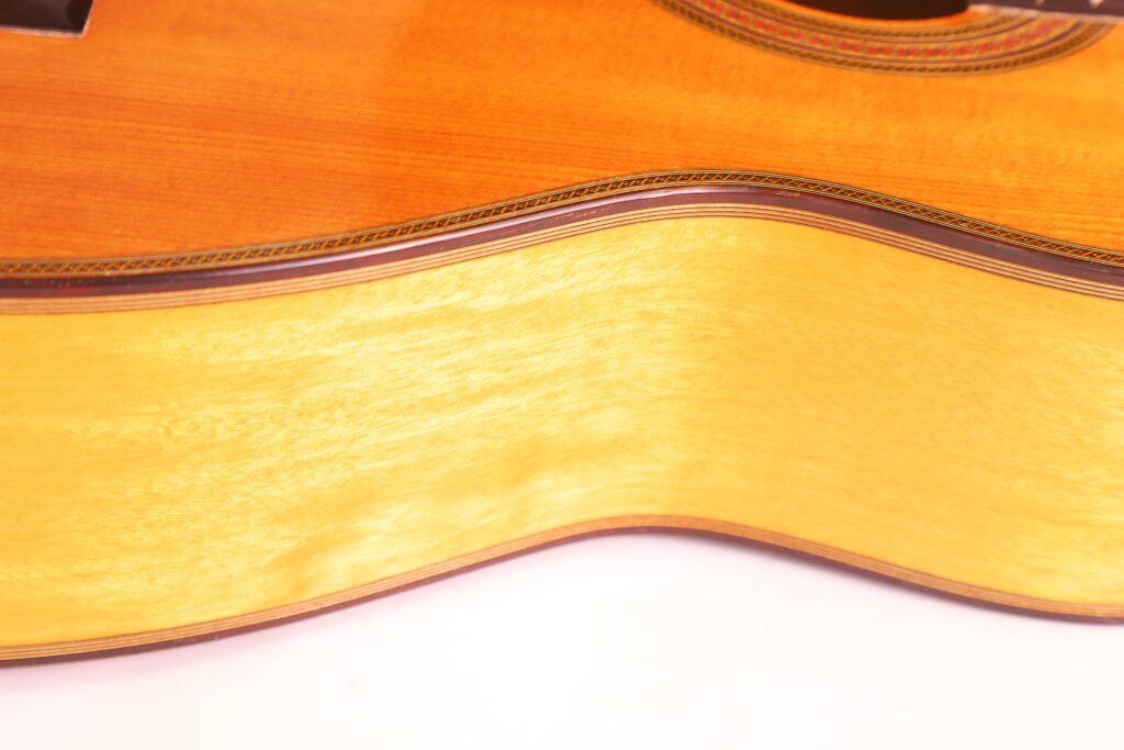 Nahaufnahme Von Zarge Und Korpus Einer Michael Wichmann 2017 Simplicio Klassische Gitarre. Hervorzuheben Sind Die Holzmaserung, Die Glänzende Oberfläche Und Ein Teil Des Schalllochs Mit Dekorativer Einlage Oben Rechts.