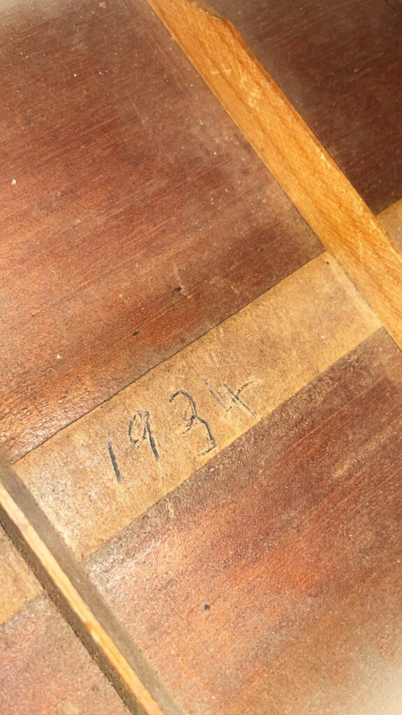 Nahaufnahme Der Hölzernen Oberfläche Der Gibson L-00 1934 Akustikgitarre, Auf Der Mit Bleistift Auf Einem Hellen Streifen Die Jahreszahl 1934&Quot; Handschriftlich Eingetragen Ist, Eingerahmt Von Dunklerem Holz Und Beleuchtet Von Warmem Licht.