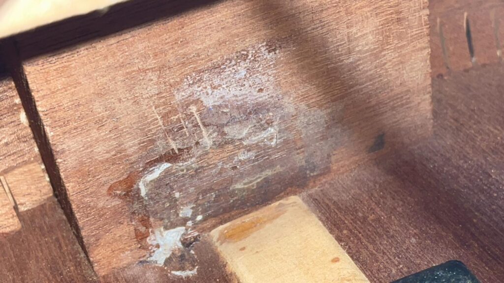 Nahaufnahme Der Holzoberfläche Der Gibson J-45 1957 Akustik Gitarre, Die Einen Rauen, Fleckigen Bereich Mit Weißen Rückständen - Möglicherweise Leim Oder Beschädigungen - Aufweist, Der Von Abschnitten Mit Unbearbeitetem Und Bearbeitetem Holz Kontrastiert Wird.