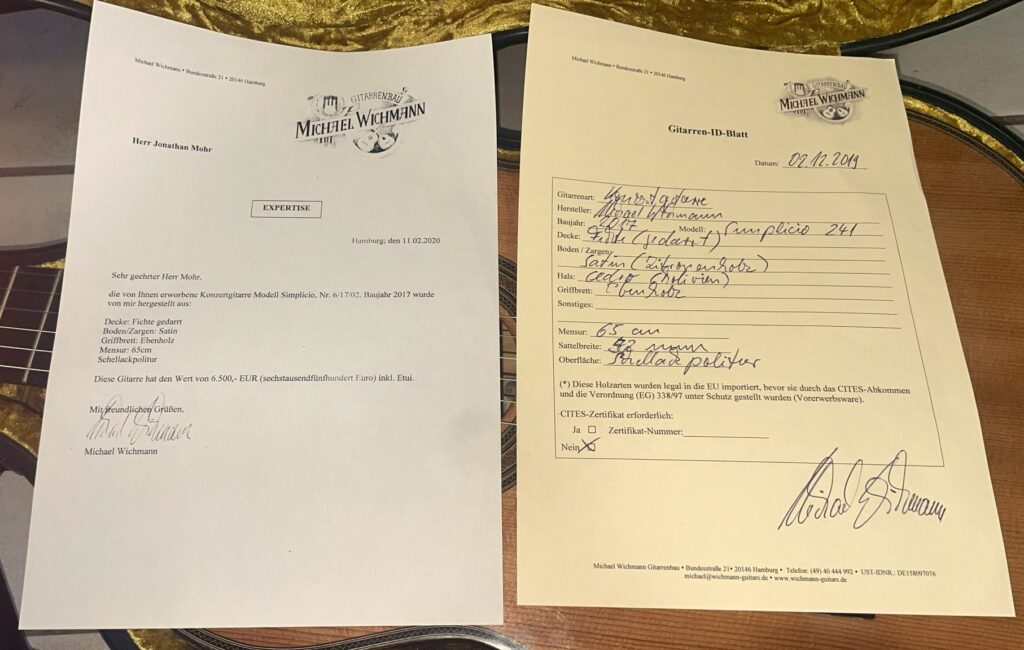 Zwei Dokumente Mit Briefköpfen Des Gitarrenstudios Michael Weishamm Liegen Auf Einer Gitarre. Links Ein Maschinengeschriebener Brief Auf Deutsch, Rechts Ein Handschriftliches Formular Mit Angaben Zu Einer Michael Wichmann 2017 Simplicio Klassische Gitarre, Datiert 02.08.2019.