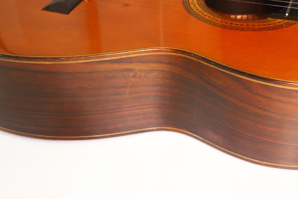 Detailansicht der Seite und des Korpus der „Ignacio Fleta 1992 Klassische Gitarre“, die die Maserung des Holzes und die eleganten Rundungen vor weißem Hintergrund hervorhebt. Detailansicht der Seite und des Korpus der „Ignacio Fleta 1992 Klassische Gitarre“, die die Maserung des Holzes und die eleganten Rundungen vor weißem Hintergrund hervorhebt.