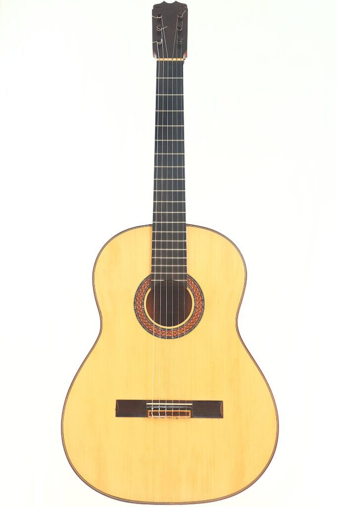 Eine Hermanos Conde 1988 Faustino Conde Flamenco Gitarre mit hellem Korpus, dunklem Griffbrett, sechs Saiten und einer dekorativen Rosette um das Schallloch ist vor weißem Hintergrund abgebildet. Eine Hermanos Conde 1988 Faustino Conde Flamenco Gitarre mit hellem Korpus, dunklem Griffbrett, sechs Saiten und einer dekorativen Rosette um das Schallloch ist vor weißem Hintergrund abgebildet.