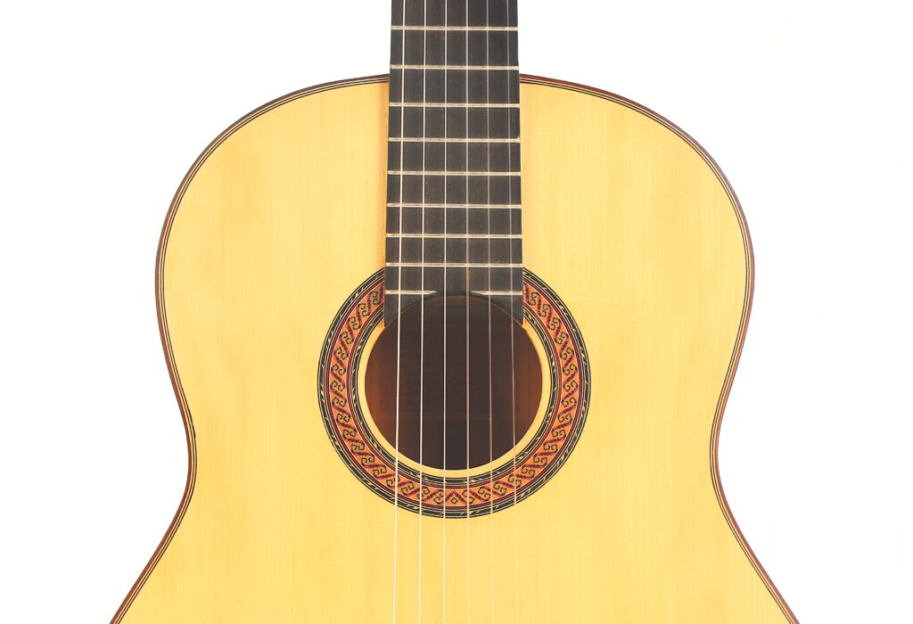 Nahaufnahme des Korpus und des Halses der „Faustino Conde Flamenco“-Gitarre von Hermanos Conde aus dem Jahr 1988, die vor weißem Hintergrund das helle Holz, die sechs Saiten und die dekorative Rosette in der Nähe des Schalllochs zeigt. Nahaufnahme des Korpus und des Halses der „Faustino Conde Flamenco“-Gitarre von Hermanos Conde aus dem Jahr 1988, die vor weißem Hintergrund das helle Holz, die sechs Saiten und die dekorative Rosette in der Nähe des Schalllochs zeigt.
