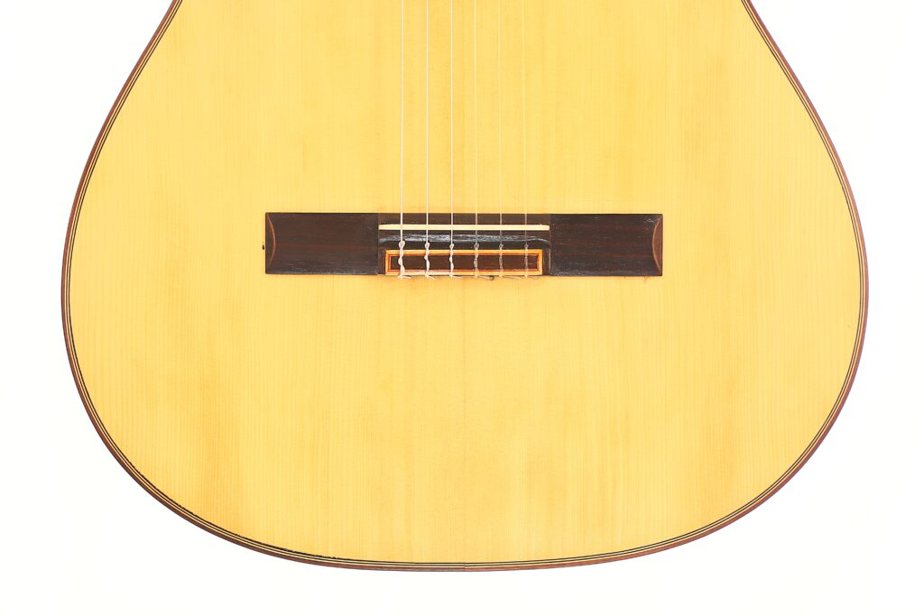 Nahaufnahme der Hermanos Conde 1988 Faustino Conde Flamenco-Gitarre, auf der die Saiten, der Steg und der helle Holzkorpus vor weißem Hintergrund zu sehen sind. Nahaufnahme der Hermanos Conde 1988 Faustino Conde Flamenco-Gitarre, auf der die Saiten, der Steg und der helle Holzkorpus vor weißem Hintergrund zu sehen sind.