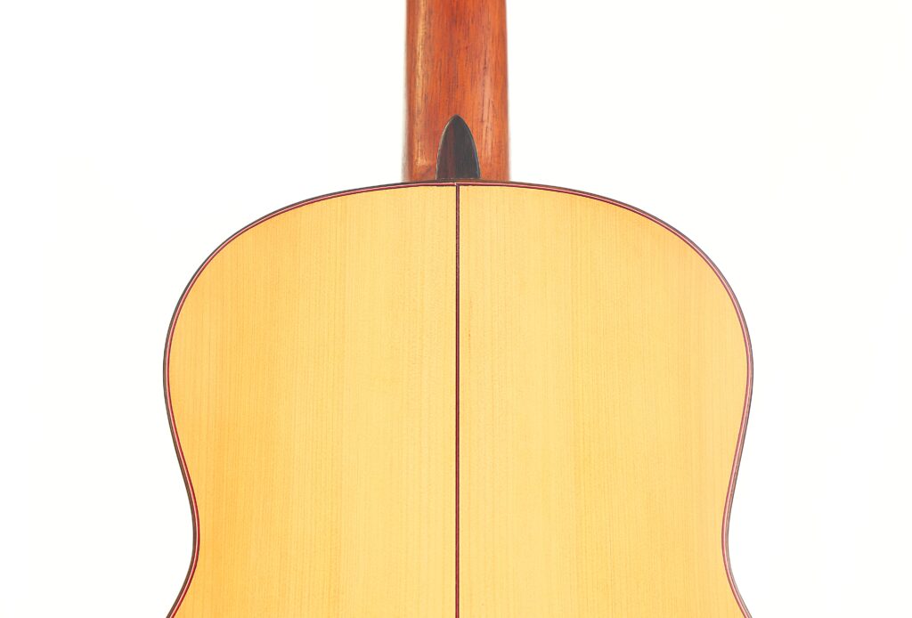 Nahaufnahme der Rückseite einer „Hermanos Conde 1988 Faustino Conde Flamenco-Gitarre“ mit einem Korpus und einem Hals aus hellem Holz sowie einer vertikalen Naht in der Mitte. Der Hintergrund ist schlicht weiß. Nahaufnahme der Rückseite einer „Hermanos Conde 1988 Faustino Conde Flamenco-Gitarre“ mit einem Korpus und einem Hals aus hellem Holz sowie einer vertikalen Naht in der Mitte. Der Hintergrund ist schlicht weiß.
