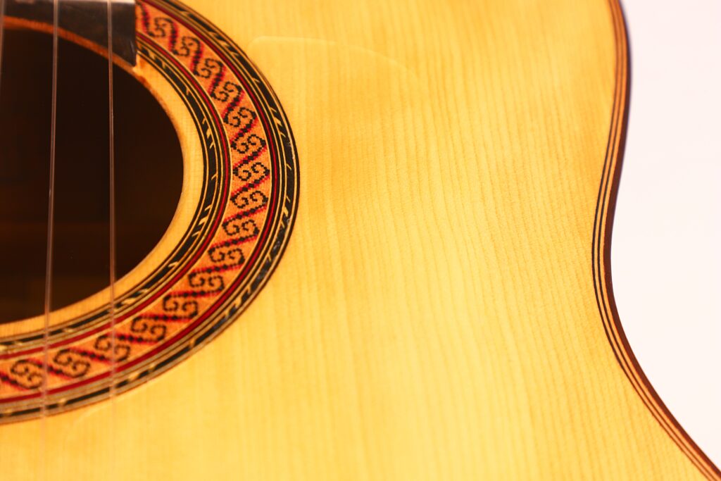 Nahaufnahme des Korpus der Hermanos Conde 1988 Faustino Conde Flamenco-Gitarre, mit Fokus auf das Schallloch mit einer rot-schwarzen Rosette auf hellem Holz. Nahaufnahme des Korpus der Hermanos Conde 1988 Faustino Conde Flamenco-Gitarre, mit Fokus auf das Schallloch mit einer rot-schwarzen Rosette auf hellem Holz.