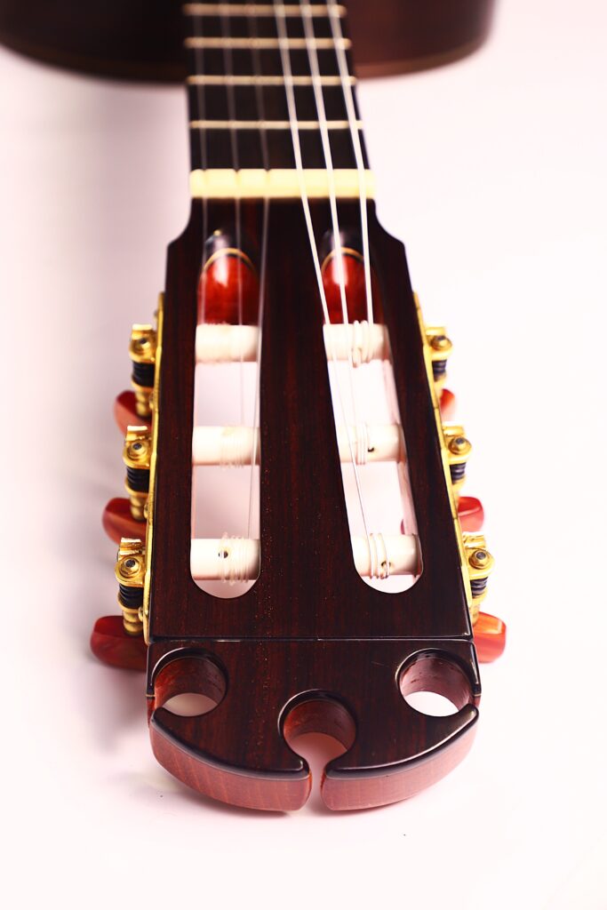 Nahaufnahme der Kopfplatte der Antonio Morales Nogués 2020 Negra Flamenco Gitarre mit Stimmwirbeln, weißen Saiten und hölzernen Details vor einem hellen Hintergrund. Nahaufnahme der Kopfplatte der Antonio Morales Nogués 2020 Negra Flamenco Gitarre mit Stimmwirbeln, weißen Saiten und hölzernen Details vor einem hellen Hintergrund.