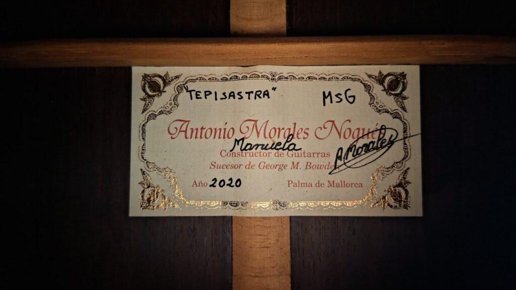 Auf dem Etikett der Antonio Morales Nogués 2020 Negra Flamenco Gitarre aus Palma de Mallorca steht: Constructor de Guitarras, Año 2020, mit den handschriftlichen Vermerken "Tepiastra", "MSG" und einem durchgestrichenen "Manuela" sowie einem verzierten Rand. Auf dem Etikett der Antonio Morales Nogués 2020 Negra Flamenco Gitarre aus Palma de Mallorca steht: Constructor de Guitarras, Año 2020, mit den handschriftlichen Vermerken "Tepiastra", "MSG" und einem durchgestrichenen "Manuela" sowie einem verzierten Rand.