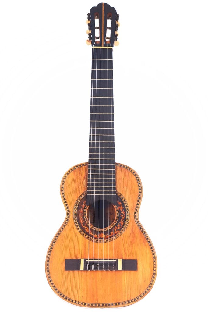 Die Vicente Carillo 1925 Terz Gitarre ist eine klassische Akustikgitarre mit einem Holzkorpus, sechs Saiten und einer detaillierten Rosette um das Schallloch, die vor einem weißen Hintergrund abgebildet ist. Die Vicente Carillo 1925 Terz Gitarre ist eine klassische Akustikgitarre mit einem Holzkorpus, sechs Saiten und einer detaillierten Rosette um das Schallloch, die vor einem weißen Hintergrund abgebildet ist.