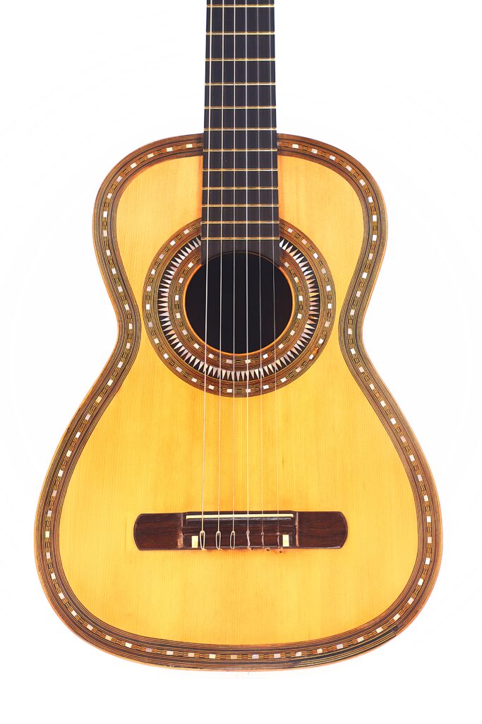 Eine Nahaufnahme der Franciso Pau 1890 Klassische Gitarre zeigt die kunstvollen Einlagen um das Schallloch und die Ränder sowie die Saiten, den Steg und das Griffbrett vor einem weißen Hintergrund. Eine Nahaufnahme der Franciso Pau 1890 Klassische Gitarre zeigt die kunstvollen Einlagen um das Schallloch und die Ränder sowie die Saiten, den Steg und das Griffbrett vor einem weißen Hintergrund.