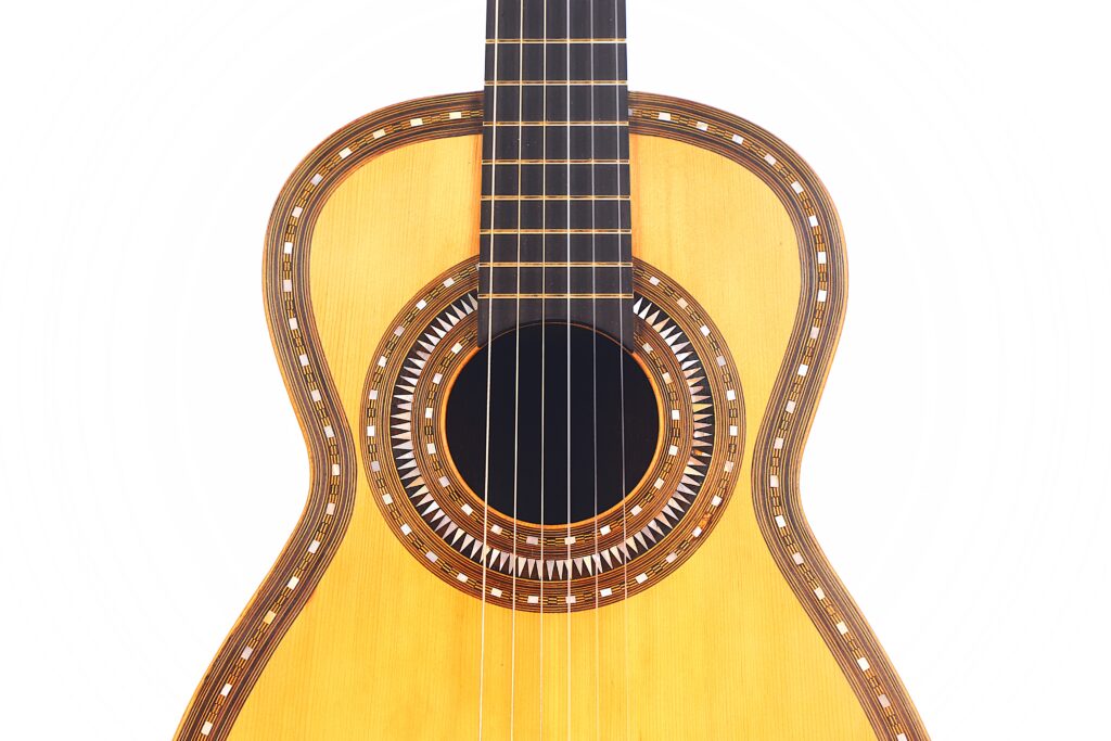 Nahaufnahme des Korpus und des Halses einer Franciso Pau 1890 Klassische Gitarre mit aufwändigen Ziereinlagen um das Schallloch und an den Rändern auf weißem Hintergrund. Nahaufnahme des Korpus und des Halses einer Franciso Pau 1890 Klassische Gitarre mit aufwändigen Ziereinlagen um das Schallloch und an den Rändern auf weißem Hintergrund.