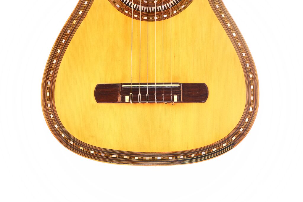 Nahaufnahme der unteren Hälfte einer Franciso Pau 1890 Klassische Gitarre mit Holzkorpus, Zierleiste, sechs Saiten und dunklem Steg vor weißem Hintergrund. Nahaufnahme der unteren Hälfte einer Franciso Pau 1890 Klassische Gitarre mit Holzkorpus, Zierleiste, sechs Saiten und dunklem Steg vor weißem Hintergrund.