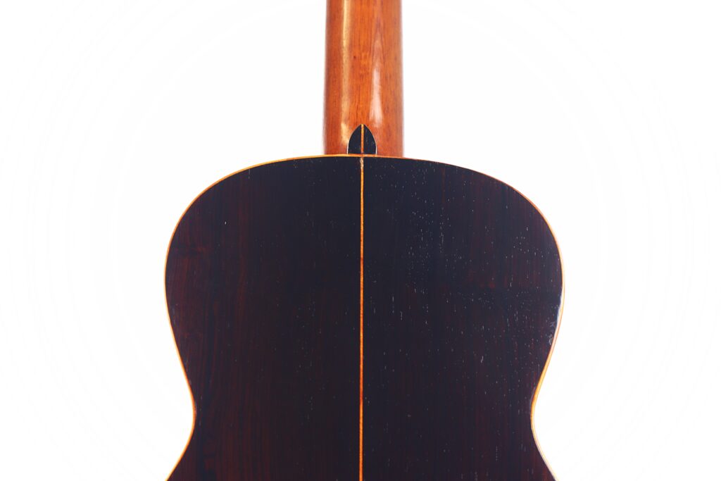 Eine Nahaufnahme der Franciso Pau 1890 Klassische Gitarre zeigt den polierten Boden aus dunklem Holz mit einem schmalen, hellen Mittelstreifen und einem passenden, nach oben reichenden Holzhals. Eine Nahaufnahme der Franciso Pau 1890 Klassische Gitarre zeigt den polierten Boden aus dunklem Holz mit einem schmalen, hellen Mittelstreifen und einem passenden, nach oben reichenden Holzhals.