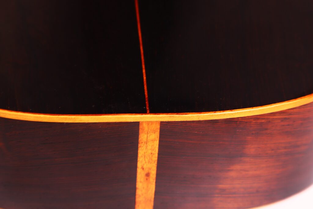 Nahaufnahme der Rückseite der Franciso Pau 1890 Klassische Gitarre. Das dunkle Holz mit der vertikalen hellen Intarsienleiste entlang der Kante zeigt die außergewöhnliche Handwerkskunst. Nahaufnahme der Rückseite der Franciso Pau 1890 Klassische Gitarre. Das dunkle Holz mit der vertikalen hellen Intarsienleiste entlang der Kante zeigt die außergewöhnliche Handwerkskunst.