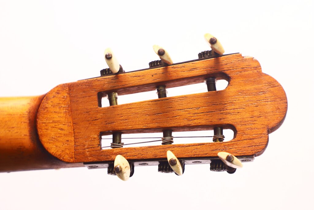 Nahaufnahme der Kopfplatte der Vicente Carrillo 1925 Terz Gitarre mit hölzernen Mechaniken und polierten Stimmwirbeln vor weißem Hintergrund. Das Holz weist eine warme, glänzende Oberfläche auf. Nahaufnahme der Kopfplatte der Vicente Carrillo 1925 Terz Gitarre mit hölzernen Mechaniken und polierten Stimmwirbeln vor weißem Hintergrund. Das Holz weist eine warme, glänzende Oberfläche auf.