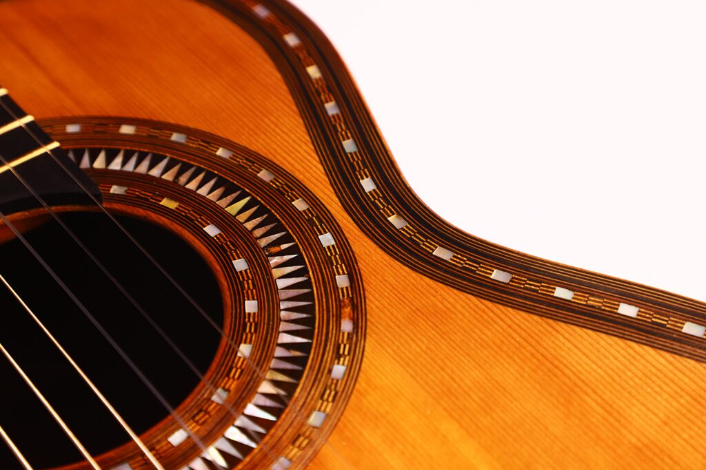 Nahaufnahme des Korpus der Franciso Pau 1890 Klassische Gitarre, mit Hervorhebung des Schalllochs, der Saiten und der detaillierten Ziereinlage entlang des Randes vor einem weißen Hintergrund. Nahaufnahme des Korpus der Franciso Pau 1890 Klassische Gitarre, mit Hervorhebung des Schalllochs, der Saiten und der detaillierten Ziereinlage entlang des Randes vor einem weißen Hintergrund.