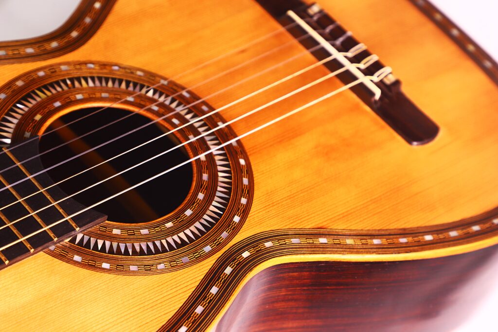 Nahaufnahme des Korpus der Franciso Pau 1890 Klassische Gitarre mit dem Schallloch mit Ziereinlage, sechs Saiten und einem Teil des Stegs vor weißem Hintergrund. Nahaufnahme des Korpus der Franciso Pau 1890 Klassische Gitarre mit dem Schallloch mit Ziereinlage, sechs Saiten und einem Teil des Stegs vor weißem Hintergrund.