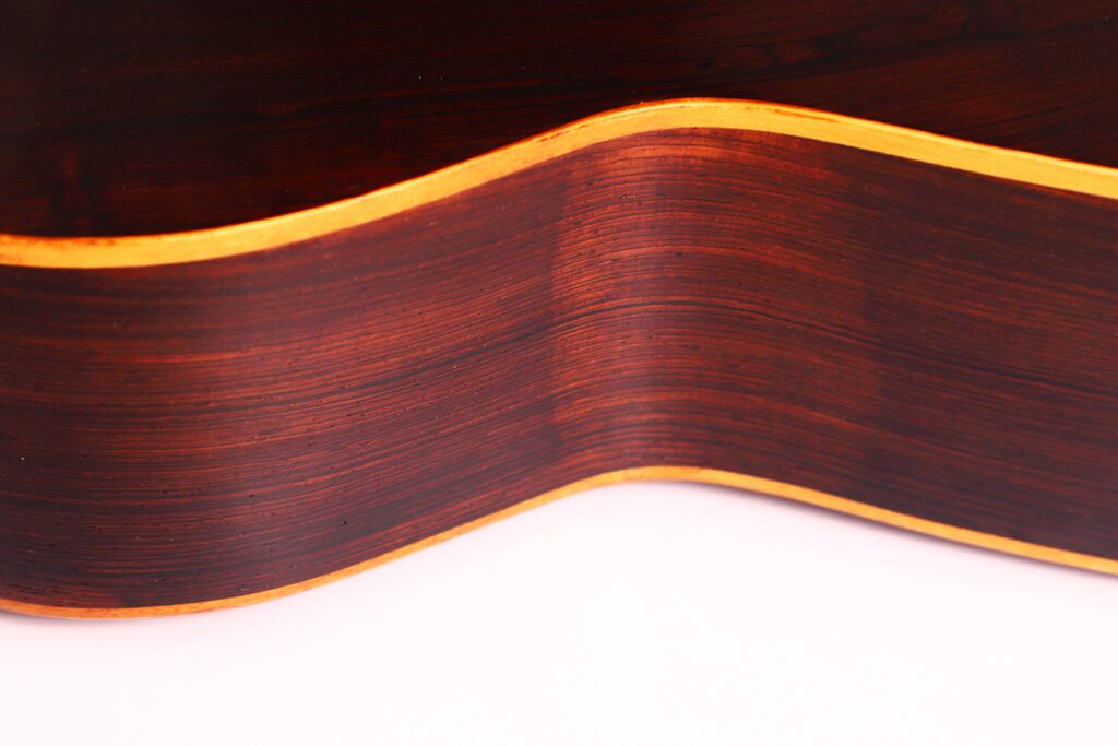Nahaufnahme der gewölbten Seite der Franciso Pau 1890 Klassische Gitarre, die die Holzmaserung, die glatte, glänzende Oberfläche und die helle Kante vor einem weißen Hintergrund hervorhebt. Nahaufnahme der gewölbten Seite der Franciso Pau 1890 Klassische Gitarre, die die Holzmaserung, die glatte, glänzende Oberfläche und die helle Kante vor einem weißen Hintergrund hervorhebt.