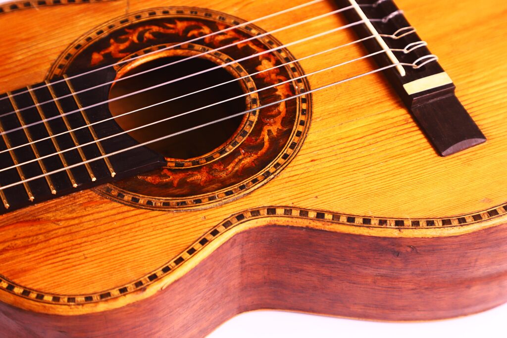 Nahaufnahme einer Terzgitarre von Vicente Carillo aus dem Jahr 1925. Hervorzuheben sind der Holzkorpus, die Zierrosette um das Schallloch, der Steg und die Saiten. Die feine Holzmaserung und die detaillierten Einlegearbeiten sind deutlich sichtbar. Nahaufnahme einer Terzgitarre von Vicente Carillo aus dem Jahr 1925. Hervorzuheben sind der Holzkorpus, die Zierrosette um das Schallloch, der Steg und die Saiten. Die feine Holzmaserung und die detaillierten Einlegearbeiten sind deutlich sichtbar.