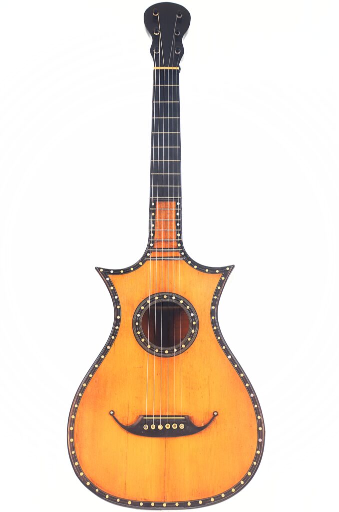 Die C.F. Marchal 1820 Romantikgitarre ist eine Vintage-Akustikgitarre mit einem einzigartig geformten hellbraunen Holzkorpus, dunklen Kanten und gepunkteten Akzenten entlang des Korpus und des Halses, fotografiert vor einem weißen Hintergrund. Die C.F. Marchal 1820 Romantikgitarre ist eine Vintage-Akustikgitarre mit einem einzigartig geformten hellbraunen Holzkorpus, dunklen Kanten und gepunkteten Akzenten entlang des Korpus und des Halses, fotografiert vor einem weißen Hintergrund.