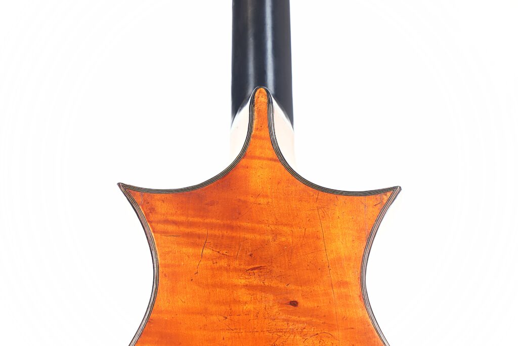 Nahaufnahme der Rückseite einer Romantikgitarre von C.F. Marchal aus dem Jahr 1820 mit einem polierten bernsteinfarbenen Holzkorpus mit einem verzierten spitzen oberen Rand und einem dunklen Hals auf weißem Hintergrund. Nahaufnahme der Rückseite einer Romantikgitarre von C.F. Marchal aus dem Jahr 1820 mit einem polierten bernsteinfarbenen Holzkorpus mit einem verzierten spitzen oberen Rand und einem dunklen Hals auf weißem Hintergrund.