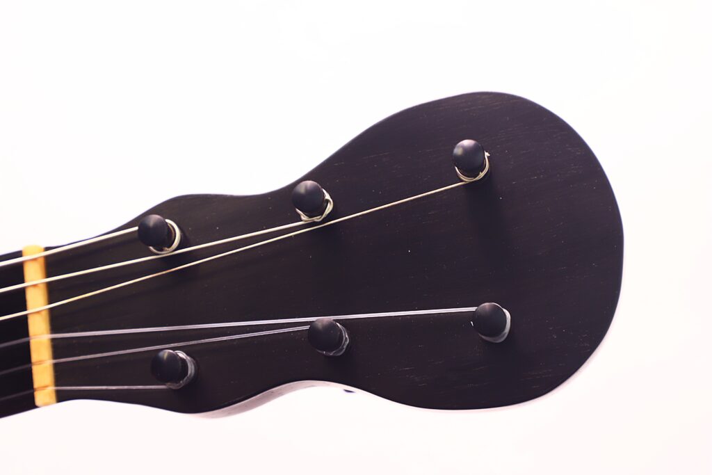 Nahaufnahme der schwarzen Kopfplatte einer C.F. Marchal 1820 Romantikgitarre, mit Stimmwirbeln und teilweise sichtbaren Saiten vor weißem Hintergrund. Nahaufnahme der schwarzen Kopfplatte einer C.F. Marchal 1820 Romantikgitarre, mit Stimmwirbeln und teilweise sichtbaren Saiten vor weißem Hintergrund.