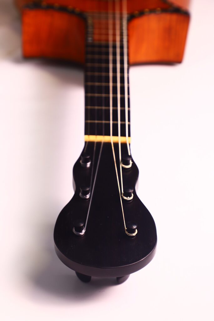 Nahaufnahme der Kopfplatte und des Halses der C.F. Marchal 1820 Romantikgitarre auf einer hellen Unterlage, wobei die Wirbel und Saiten hervorgehoben werden. Nahaufnahme der Kopfplatte und des Halses der C.F. Marchal 1820 Romantikgitarre auf einer hellen Unterlage, wobei die Wirbel und Saiten hervorgehoben werden.