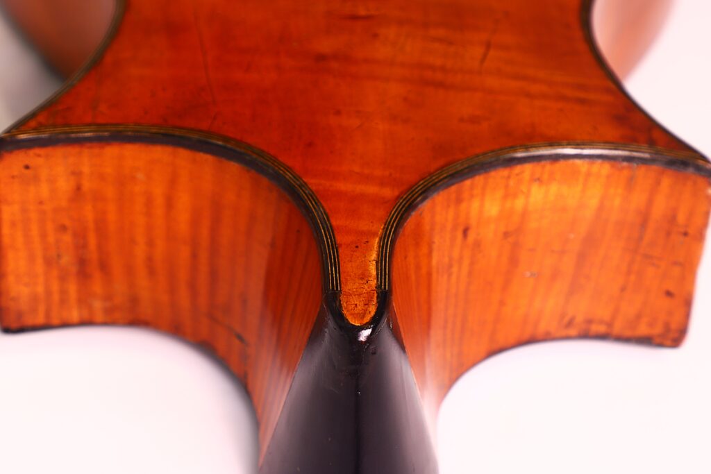 Nahaufnahme der Rückseite einer Romantikgitarre von C.F. Marchal aus dem Jahr 1820 mit zentraler Naht, glänzender orange-brauner Holzoberfläche, detaillierter Maserung und schwarzer Einfassung entlang der Rundungen. Nahaufnahme der Rückseite einer Romantikgitarre von C.F. Marchal aus dem Jahr 1820 mit zentraler Naht, glänzender orange-brauner Holzoberfläche, detaillierter Maserung und schwarzer Einfassung entlang der Rundungen.