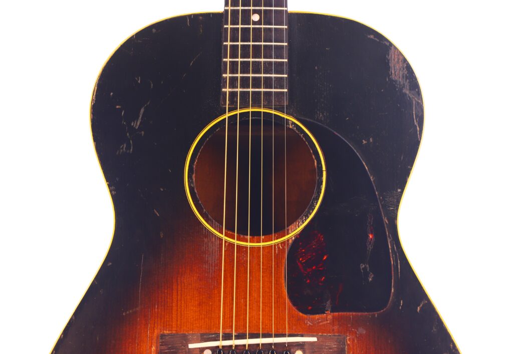 Nahaufnahme einer Gibson LG-1 1953 Akustik-Gitarre mit dunkler, abgenutzter Lackierung, gelber Schalllochblende und sichtbaren Kratzern und Schrammen im Holz. Nahaufnahme einer Gibson LG-1 1953 Akustik-Gitarre mit dunkler, abgenutzter Lackierung, gelber Schalllochblende und sichtbaren Kratzern und Schrammen im Holz.